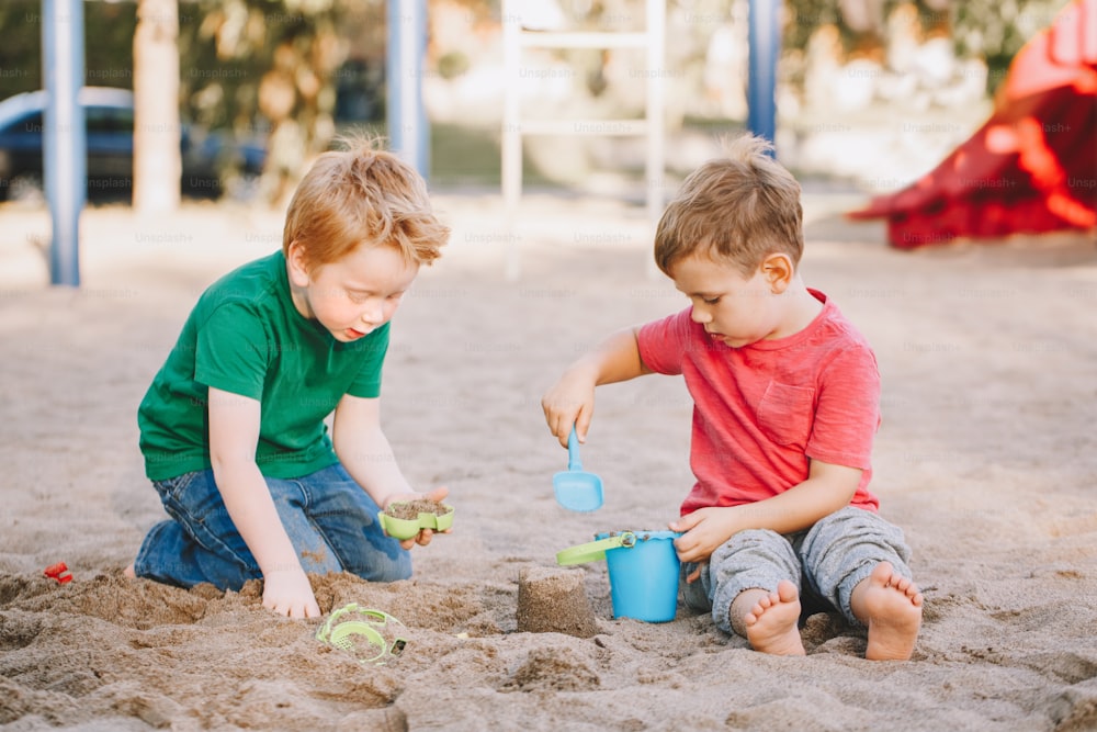 Two Caucasian children sitting in sandbox playing with beach toys. Little boys friends having fun together on playground. Summer outdoor activity for kids. Leisure time lifestyle childhood.