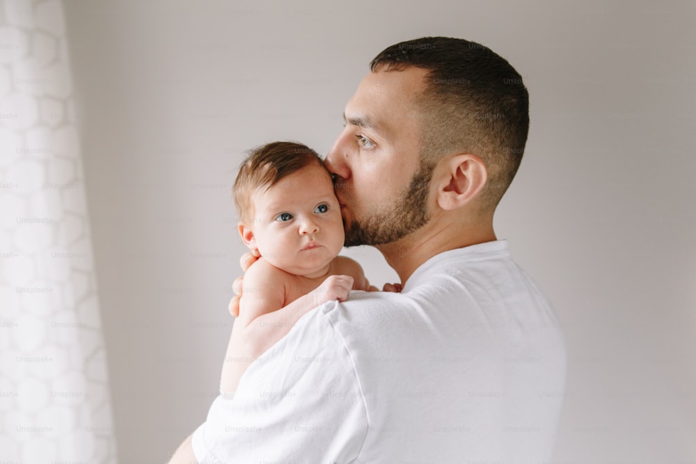 Fathers Day holiday. Bearded Caucasian father kissing newborn baby girl. Parent holding rocking child daughter son on hands. Authentic lifestyle candid moment. Young single dad family life.