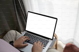 Vista de perto a jovem mulher sentada no sofá e usando o computador portátil em casa.