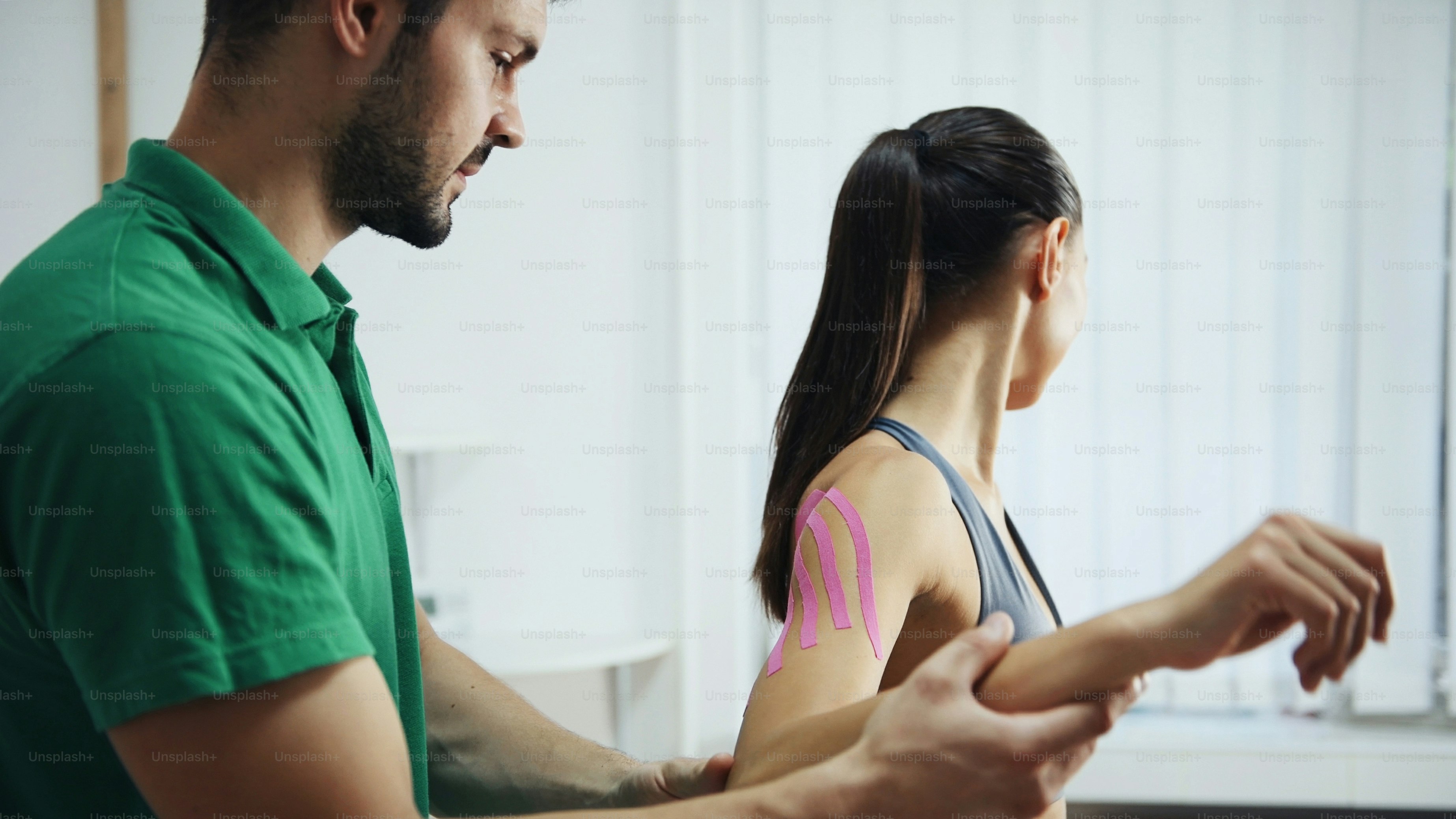 Doctor helps woman by shoulder treatment with kinesio tape.