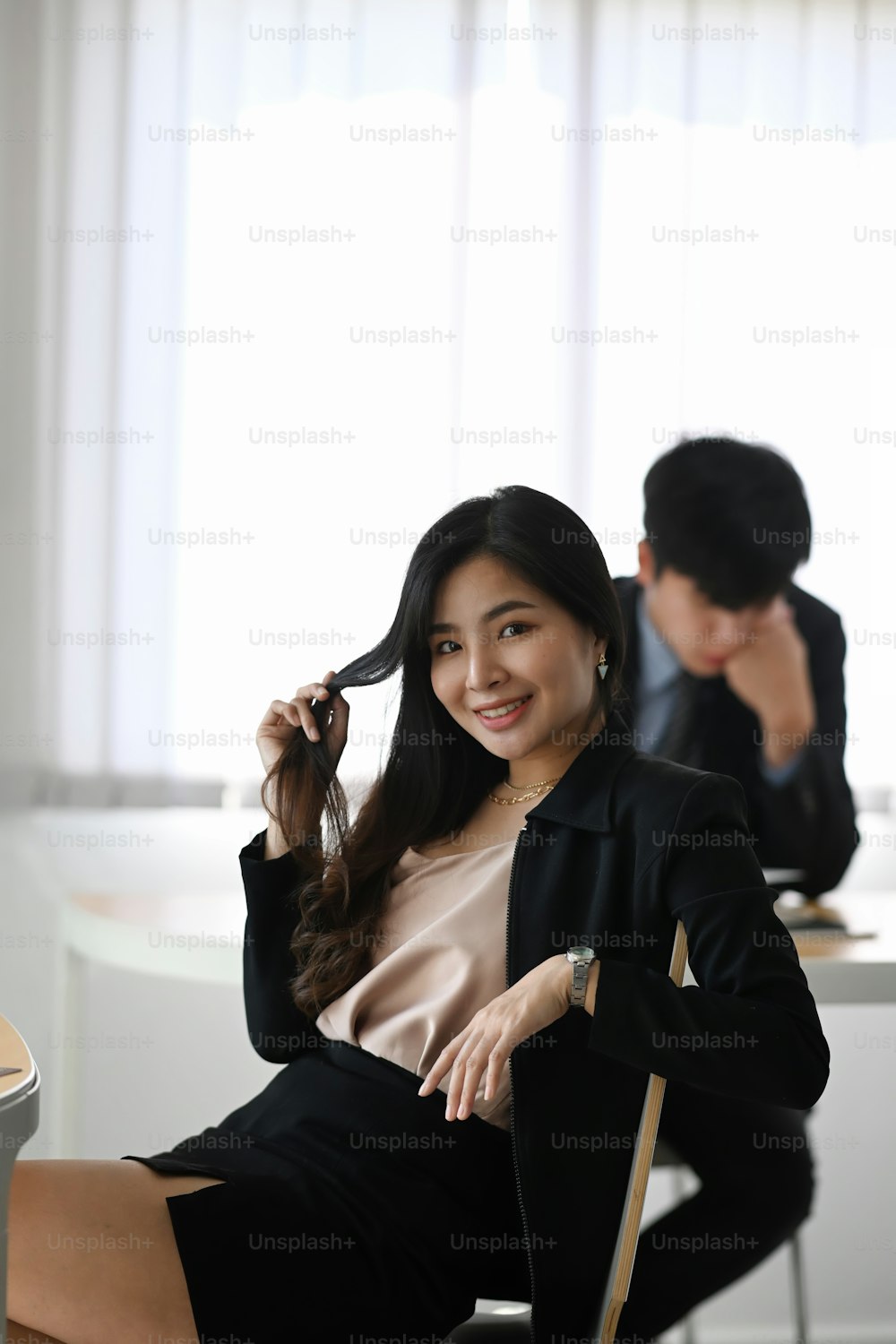 Portrait of happy businesswoman smiling to camera and sitting with her colleague in office.