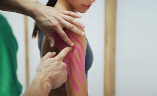 El médico ayuda a la mujer mediante el tratamiento del hombro con cinta de kinesio.