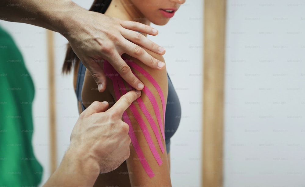 Doctor helps woman by shoulder treatment with kinesio tape.