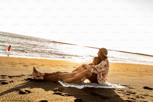 Happy family relaxing on the sandy beach during sunset. Parents lying, hugging and looking for a little daughter in the ocean. Travel lifestyle,  summer vacation.