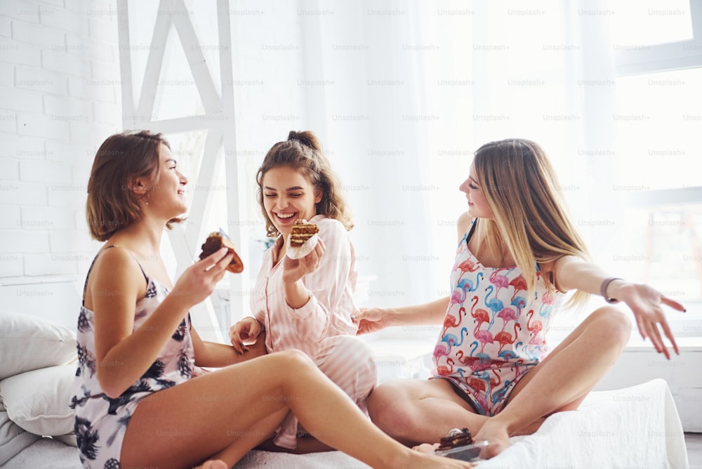 Eating sweets together. Happy female friends having good time at pajama party in the bedroom.
