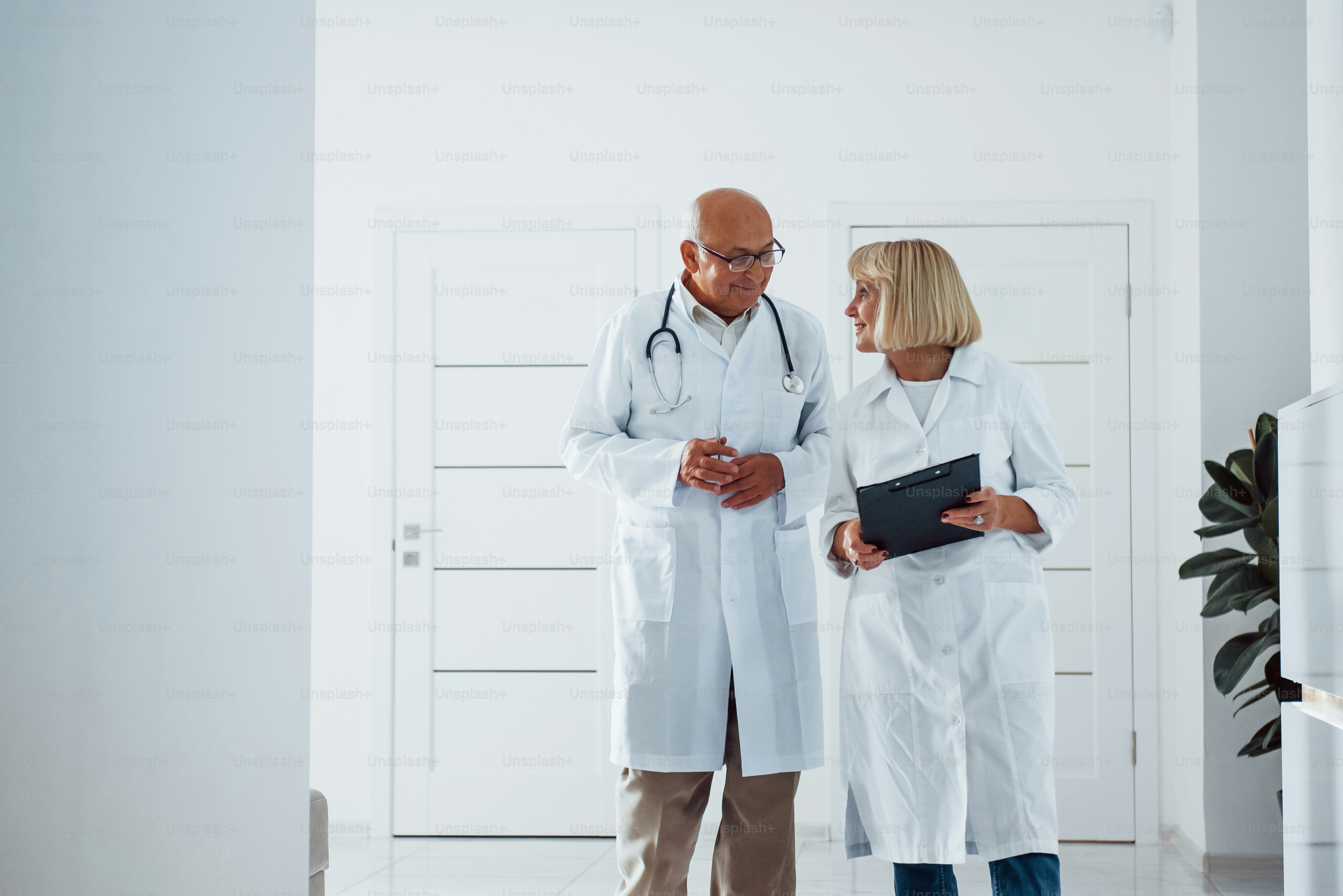 Two senior doctors stands in the clinic with notepad and talks to each ...