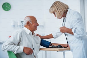Female doctor uses tonometer to make blood pressure measuring to senior man.