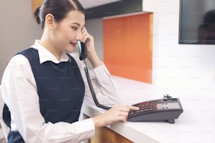 Sirvienta en uniforme azul usando el teléfono en la habitación del hotel