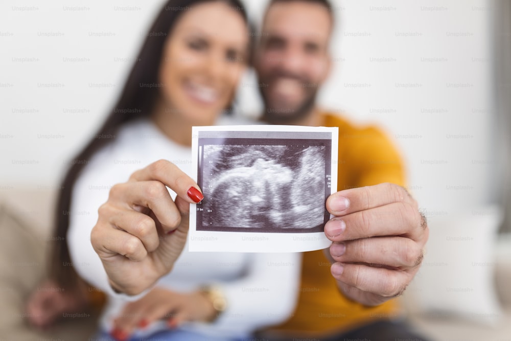 Frau und ihr Freund halten ein Bild ihres Sonogramms des Babys hoch. Junges glückliches Paar mit Baby-Ultraschallfoto