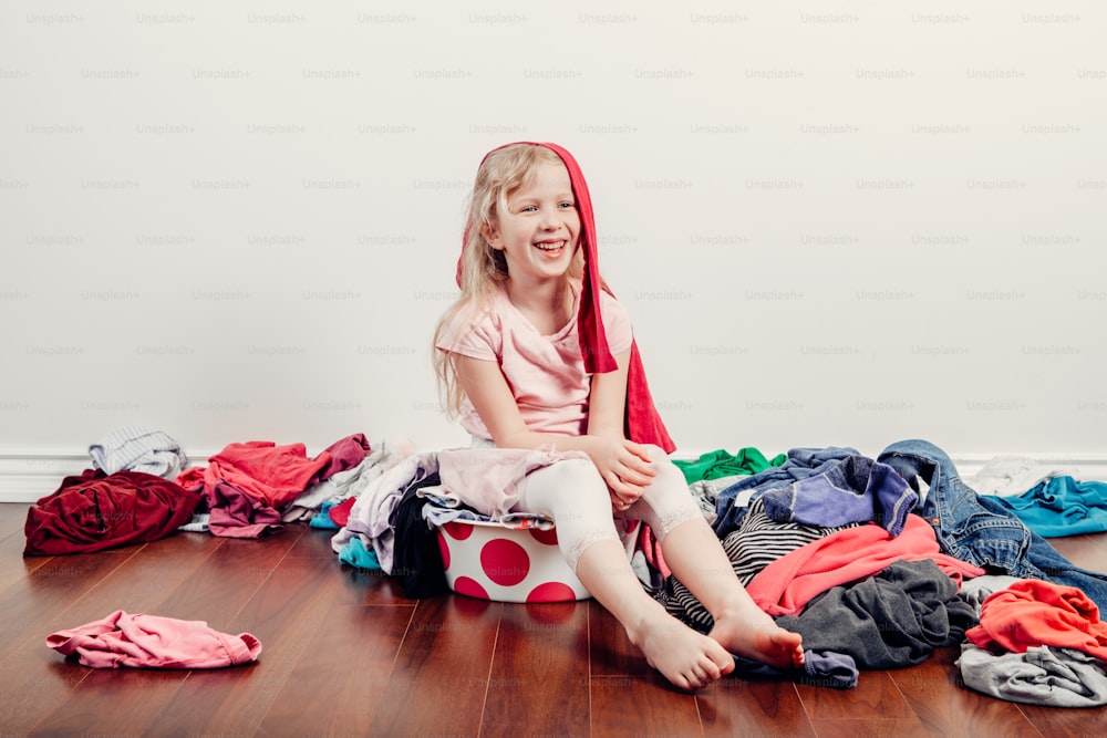 Mommy little helper. Cute Caucasian girl sorting clothes. Adorable funny child arranging organazing clothing. Kid with messy stack of clothes things on floor. Home chores housework for children.