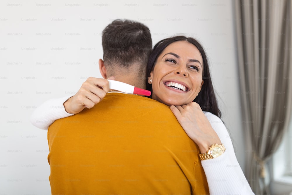 Couple with positive home pregnancy test. I'm pregnant Happy young couple with pregnancy test. Closeup of happy young woman embracing man after positive pregnancy test