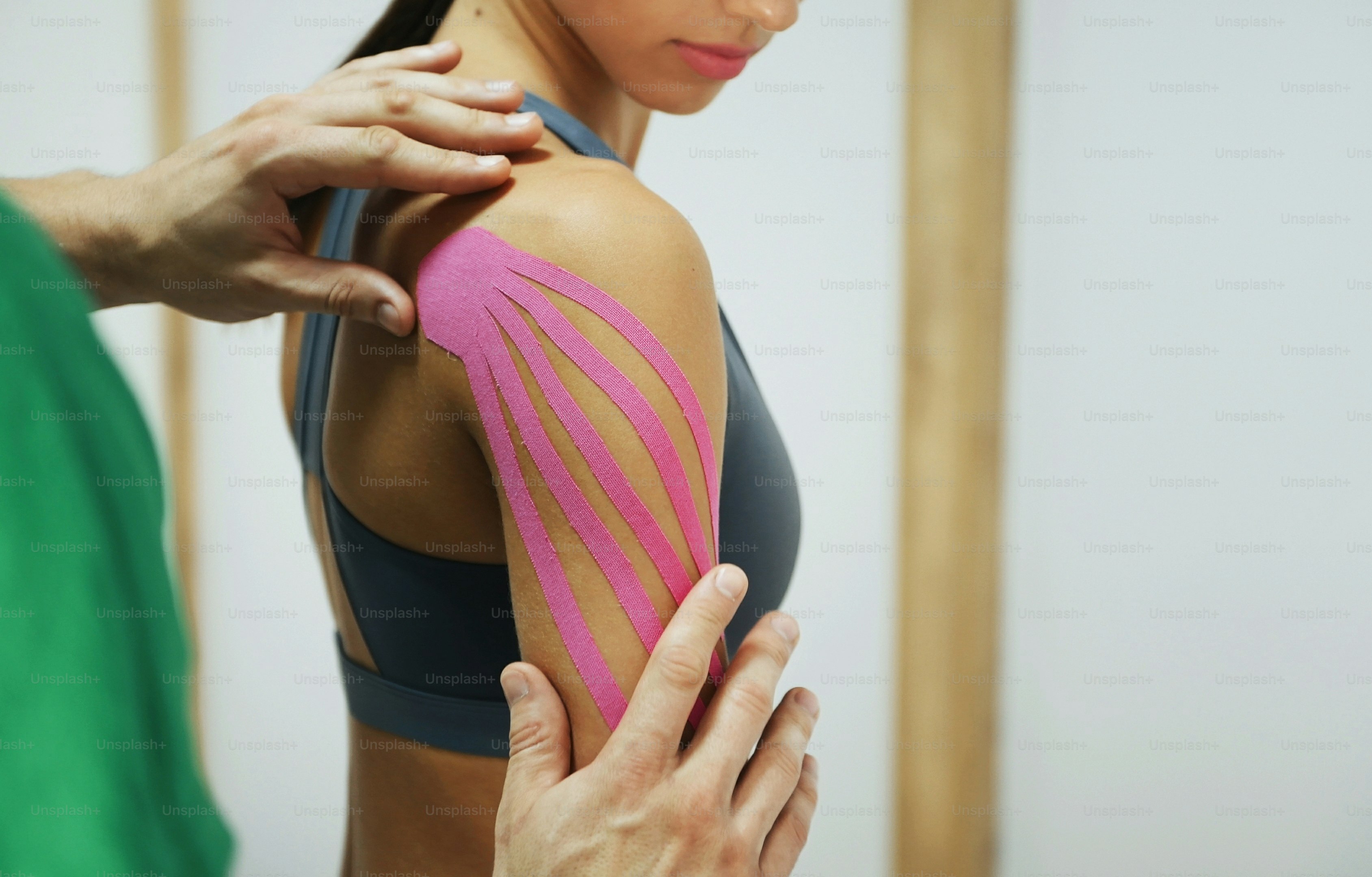 Doctor helps woman by shoulder treatment with kinesio tape.
