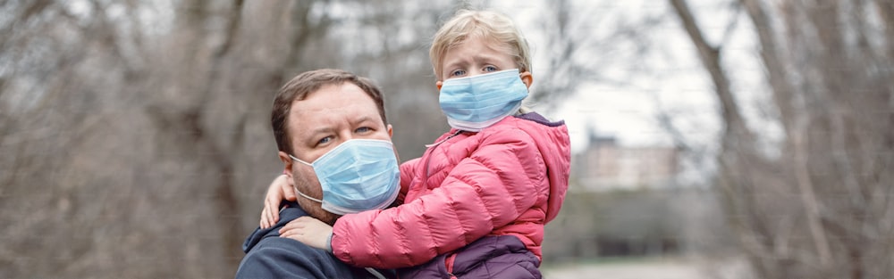 屋外で衛生的なフェイスマスクを着用した子供の女の子を持つ父親。家族のお父さんと娘は、コロナウイルスcovid-19の危険な蔓延から身を守ります。Web サイトのバナー ヘッダー。