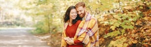 Hermosa pareja hombre mujer enamorada. Novio y novia envueltos en una manta amarilla abrazados en el parque en un día de otoño y otoño. Personas auténticas y reales. Encabezado de banner para sitio web.