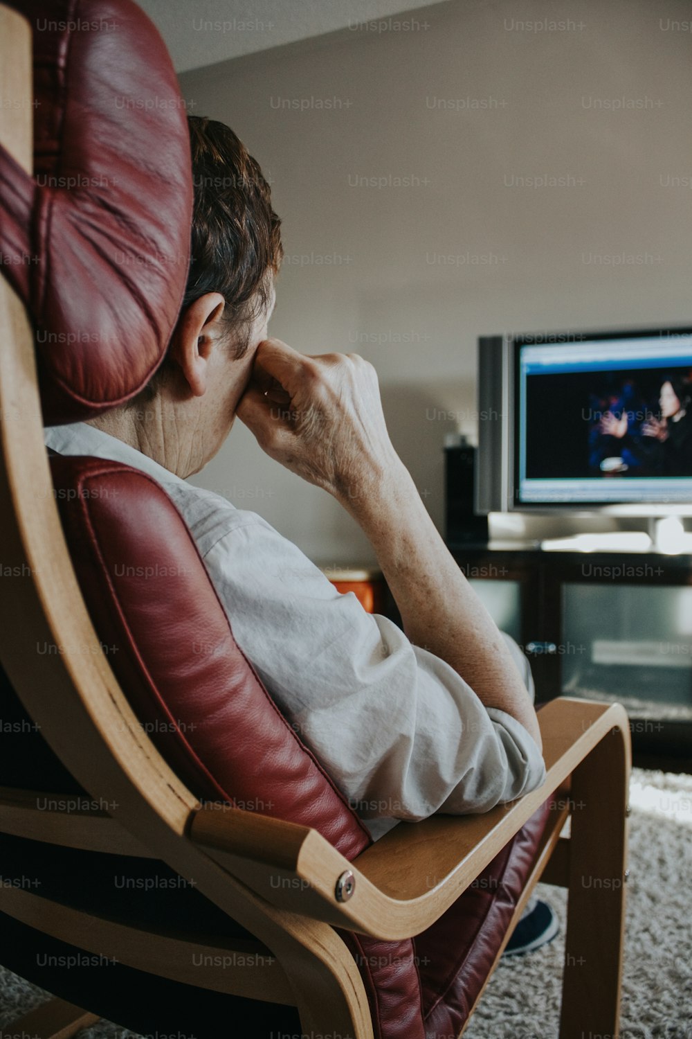 Old woman sitting in arm chair at home watching tv. Pensive mature old senior female listening to news on television. Emotional portrait of old unhappy human woman. Maturity and fake news.