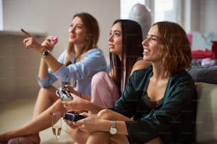 Woman with a strawberry macaron sitting on the floor by her friends playing a video game
