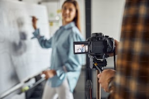 Beautiful smiling pleased dark-haired young Caucasian engineer being filmed by her colleague in the office