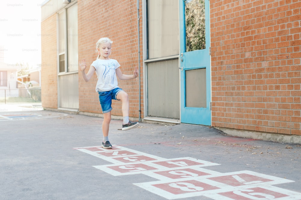 Giovane ragazza del bambino che gioca saltando la campana sul cortile della scuola all'aperto. Divertente gioco di attività per bambini nel parco giochi. Sport di strada per bambini. Stile di vita infantile felice.