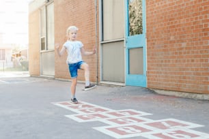 Young child girl playing jumping hopscotch on school yard outdoor. Funny activity game for kids on playground. Street sport for children. Happy childhood lifestyle.