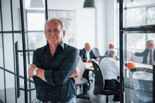 Porträt eines älteren Mannes, der vor einem älteren Team älterer Geschäftsmann-Architekten steht, die ein Meeting im Büro haben.