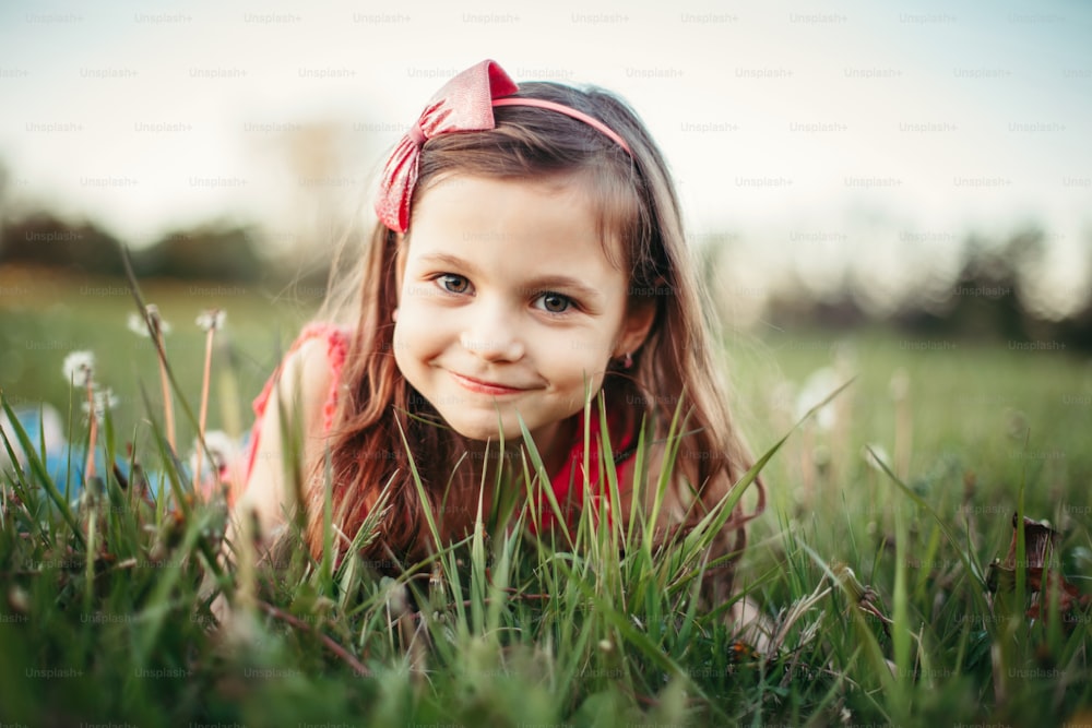 Cute adorable Caucasian girl among dandelions flowers. Child lying in grass on meadow. Outdoor fun summer seasonal children activity. Kid having fun outside. Happy childhood lifestyle.