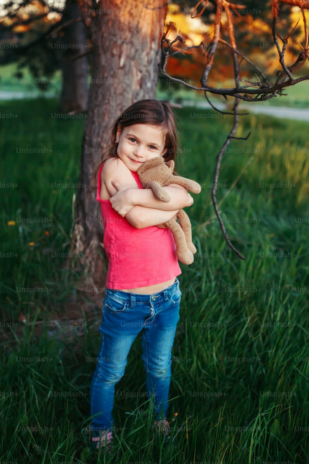 Cute adorable Caucasian girl hugging toy. Child embrace soft plush bear in park. Outdoor fun summer seasonal children activity. Kid having fun outside. Happy childhood lifestyle.