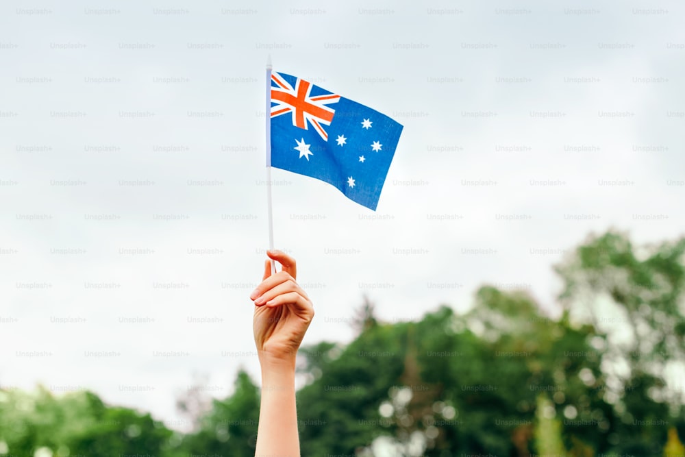 Closeup of woman human hand arm waving Australian flag against blue sky. Proud citizen man celebrating national Australia Day in January outdoor. National day holiday.