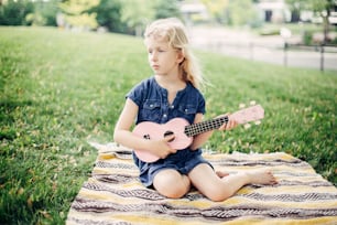 Cute adorable blonde girl playing pink guitar toy outdoor. Child playing music and singing song in park. Hobby activity for children kids. Tender memorable authentic candid childhood moment.