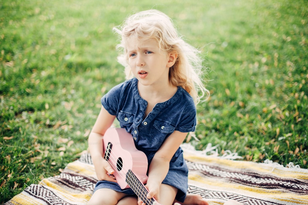 Jolie fille blonde adorable jouant un jouet de guitare rose en plein air. Enfant jouant de la musique et chantant des chansons dans le parc. Activité de loisir pour les enfants. Tendre, mémorable, authentique, candide moment d’enfance.