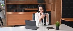 Attractive woman entrepreneur holding coffee cup and sitting in modern workplace.