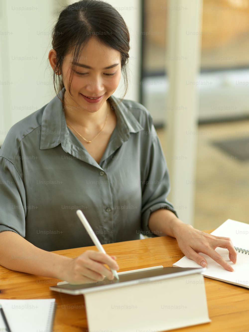 Portrait of smiling female office worker working on digital tablet with stylus pen on wooden table