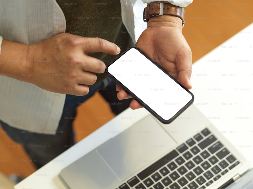 Top view of businessman using smartphone with mock up screen while standing at workspace, clipping path