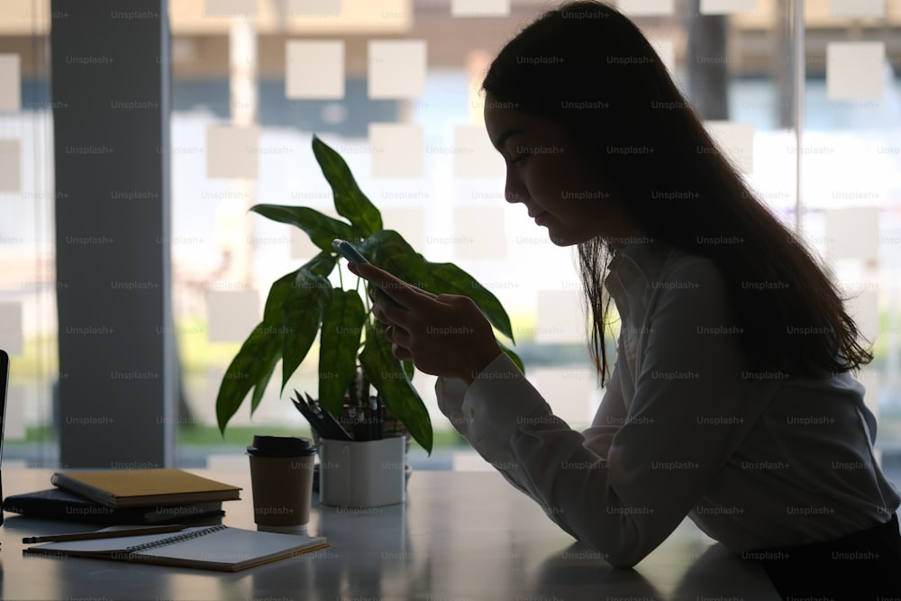 Silhouette di bella donna d'affari seduta in ufficio e utilizzando lo smartphone.