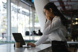 Vista lateral de una mujer de negocios emocionada leyendo buenas noticias en una computadora portátil mientras está sentada en la oficina.
