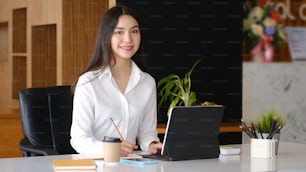 Smiling businesswoman hand holding pen and working with computer tablet at office.