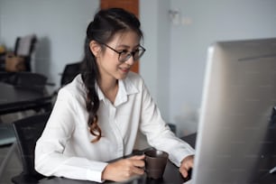 Young asian businesswoman drinking coffee and using laptop computer in office.