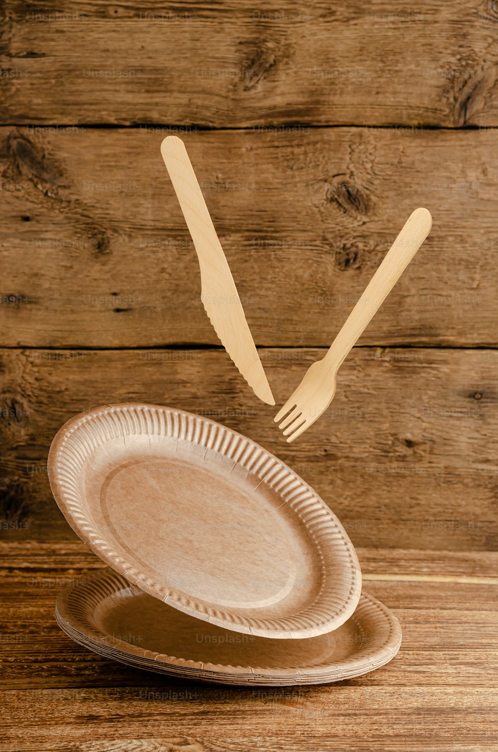 Flying disposable paper tableware on wooden background. Environmental care concept. Copy space.