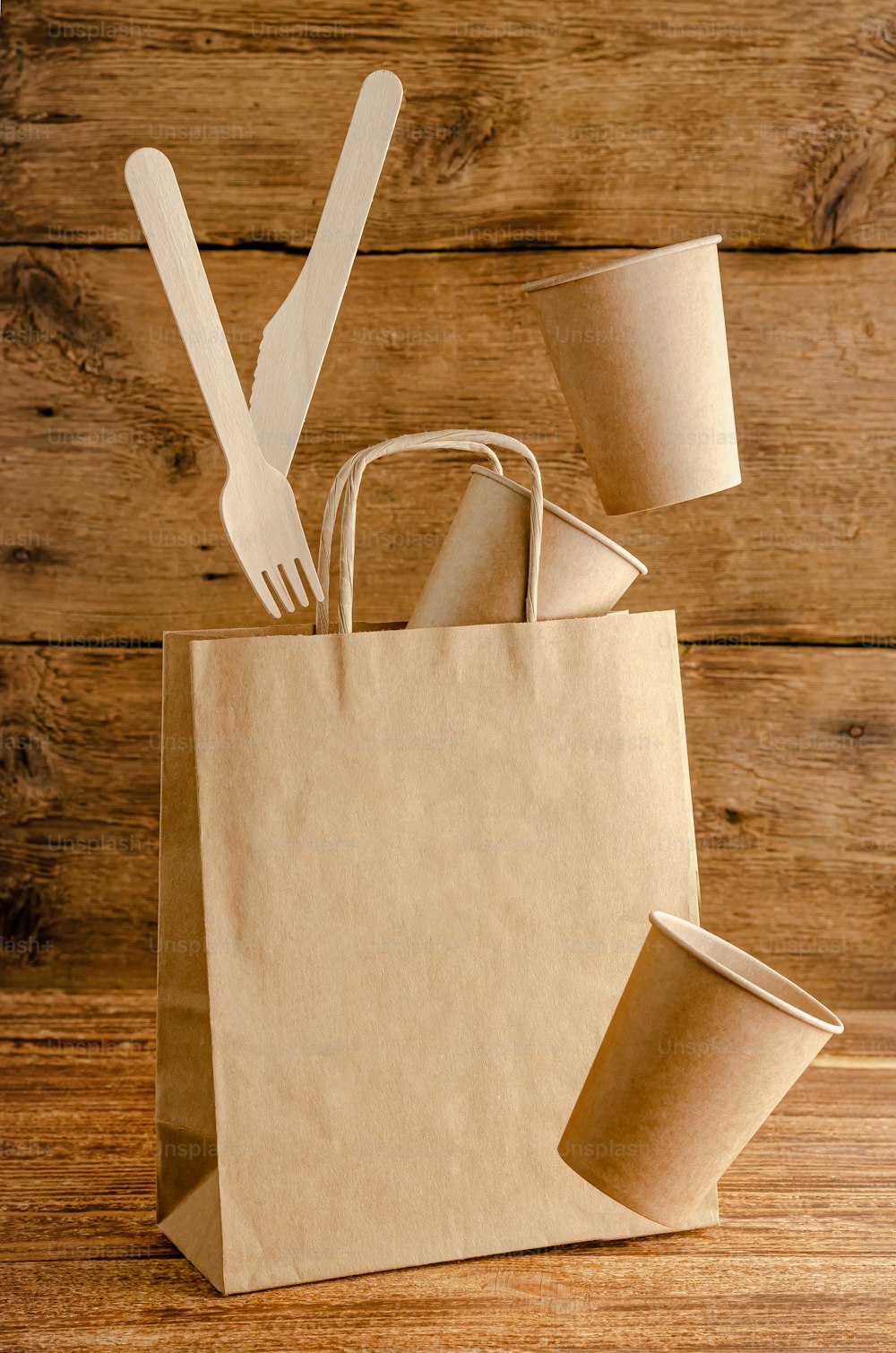 Flying disposable paper tableware over bag with mock up on wooden background. Environmental care concept.