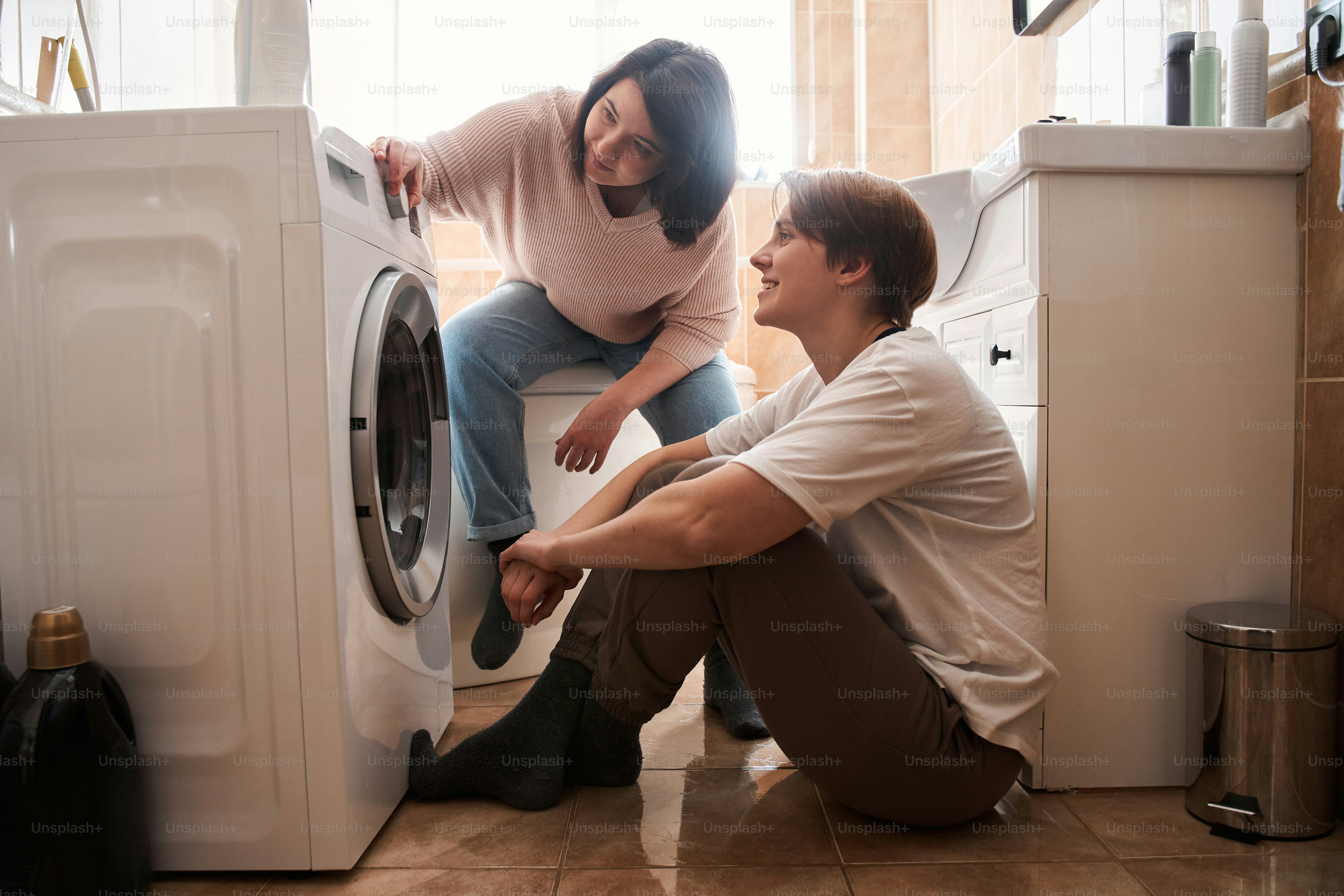 Couple de lesbiennes souriant tout en faisant la lessive ensemble près de la machine à laver. Couple lesbien LGBT moments d’amour et concept de bonheur. Banque d’images