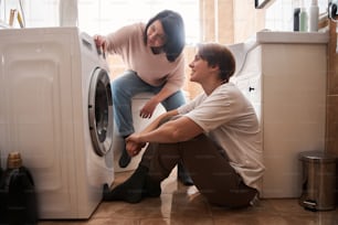 Lesbian couple smiling while doing laundry together near the washing machine. LGBT lesbian couple love moments and happiness concept. Stock photo