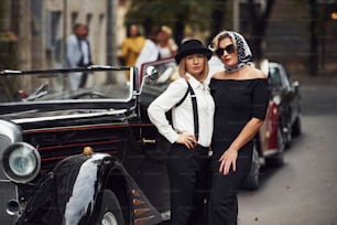 Women in old fashioned clothes stands together near retro car.