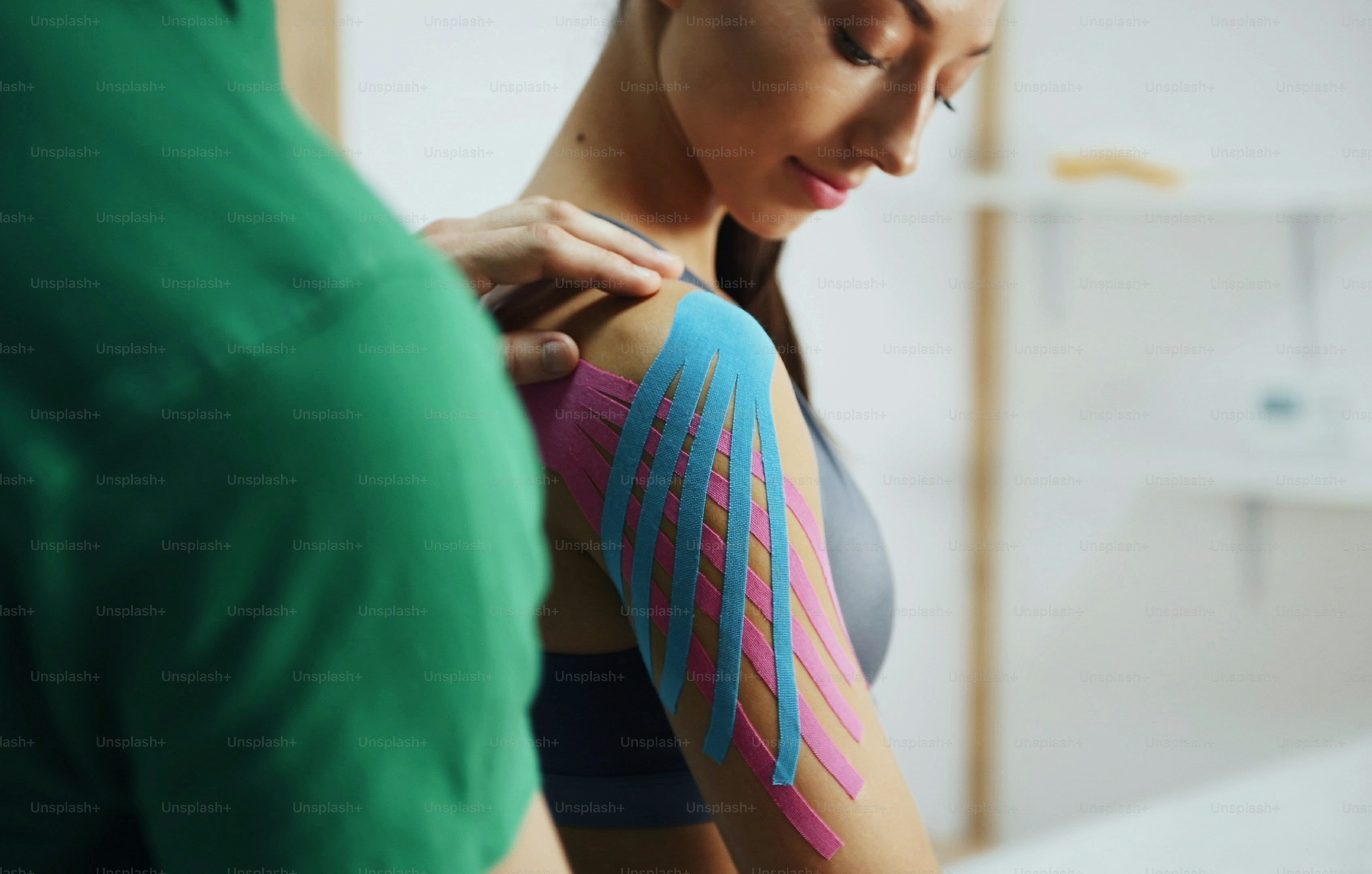 Doctor helps woman by shoulder treatment with kinesio tape.