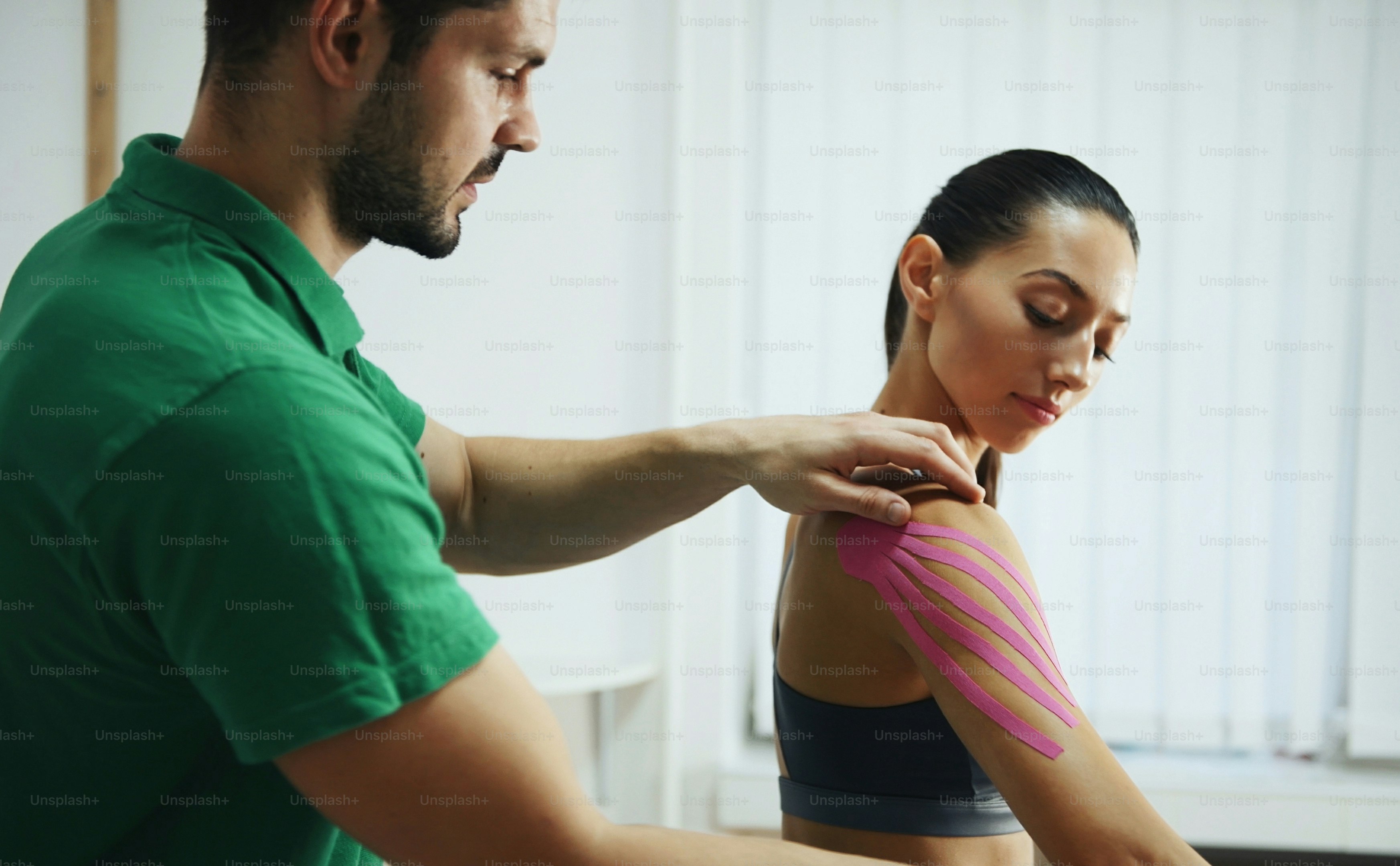 Doctor helps woman by shoulder treatment with kinesio tape.