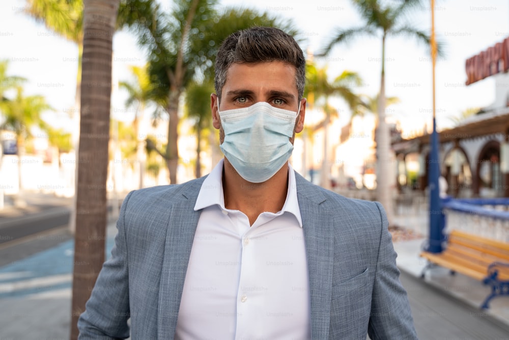 Handsome businessman with face mask for protection outdoors, looking at camera. Restrictions during pandemic.