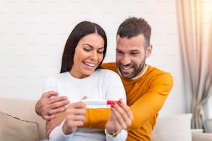 Shot of a happy couple celebrating their new pregnancy at home together. Young couple looking happy after taking a home pregnancy test. Happy couple looking at pregnancy test