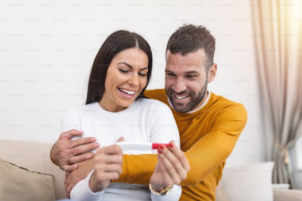 Shot of a happy couple celebrating their new pregnancy at home together. Young couple looking happy after taking a home pregnancy test. Happy couple looking at pregnancy test