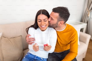 Young couple is happy because of positive pregnancy test. Affectionate couple finding out results of a pregnancy test in their home. Family, parenting and medical concept