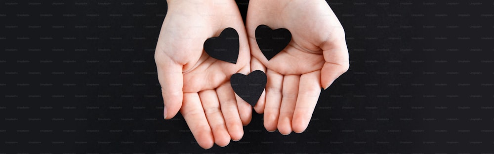 Hands holding black paper hearts on dark background. Support of USA movement protests. People protest against racism. Blackout Tuesday 2020. Banner header for website.