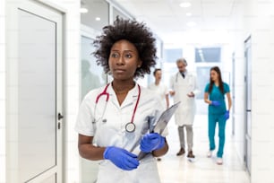 Serious African American female doctor walking with patient's test results before meeting with the patient. The doctor is in a hospital hallway.