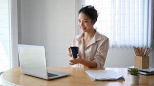 Alegre mujer de negocios sosteniendo una taza de café y usando una computadora portátil haciendo videollamadas con colegas.